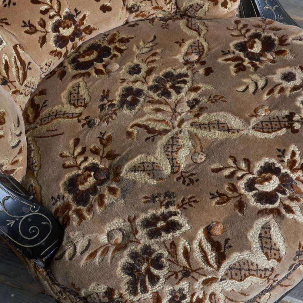 A Victorian low-seated tub chair upholstered in brown patterned floral velvet with ebonised turned legs, gilt accents, and brass castors. View IX