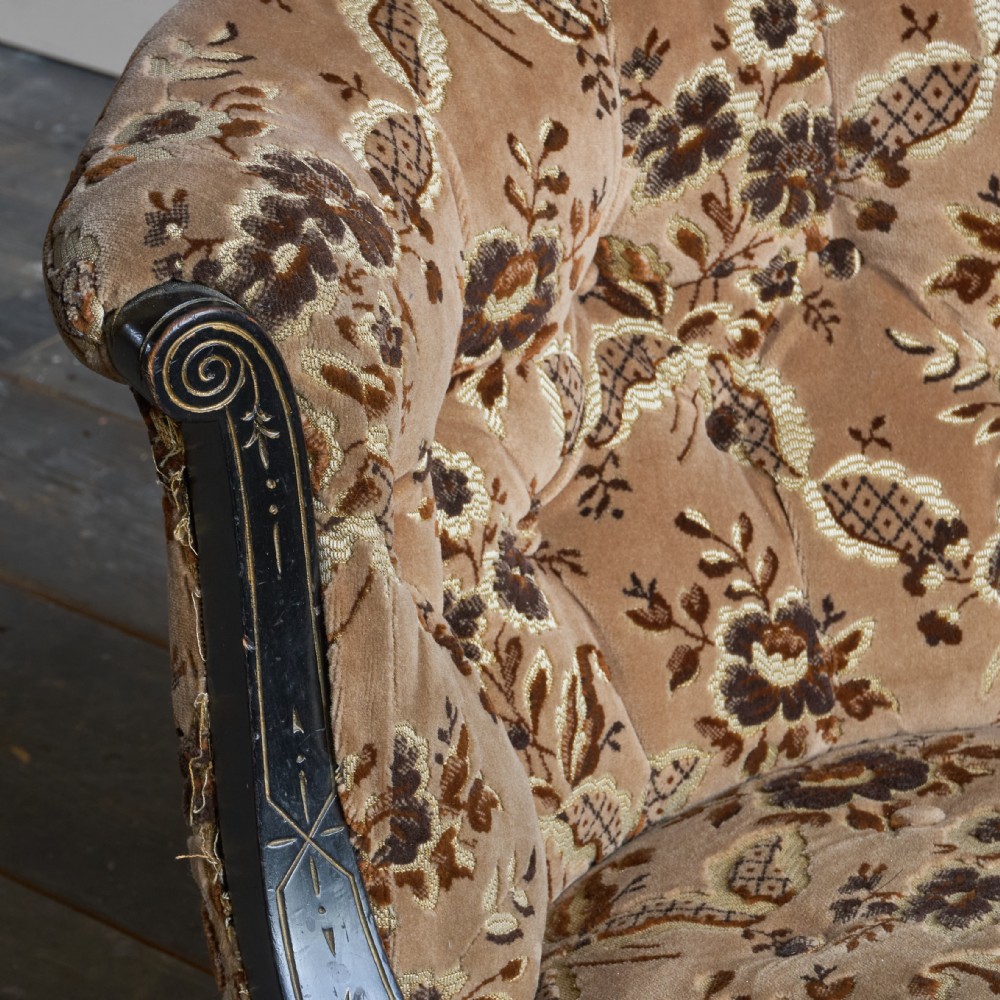 A Victorian low-seated tub chair upholstered in brown patterned floral velvet with ebonised turned legs, gilt accents, and brass castors. View X
