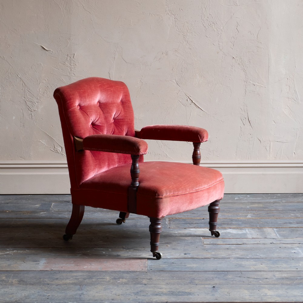 Victorian open armchair featuring deep buttoned rose pink velvet upholstery, turned wooden front legs, and brass castors. View II