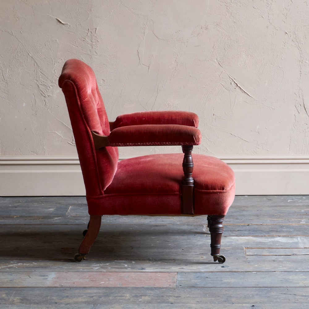 Victorian open armchair featuring deep buttoned rose pink velvet upholstery, turned wooden front legs, and brass castors. View IV