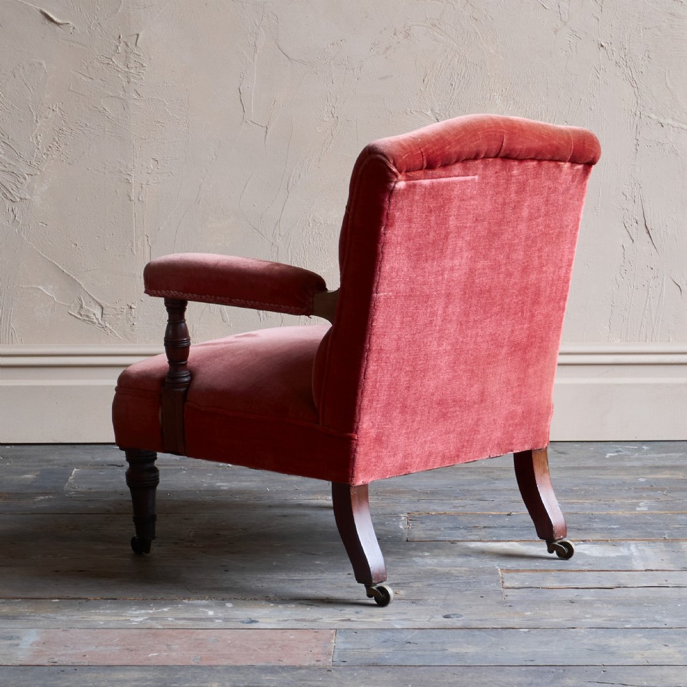 Victorian open armchair featuring deep buttoned rose pink velvet upholstery, turned wooden front legs, and brass castors. View V