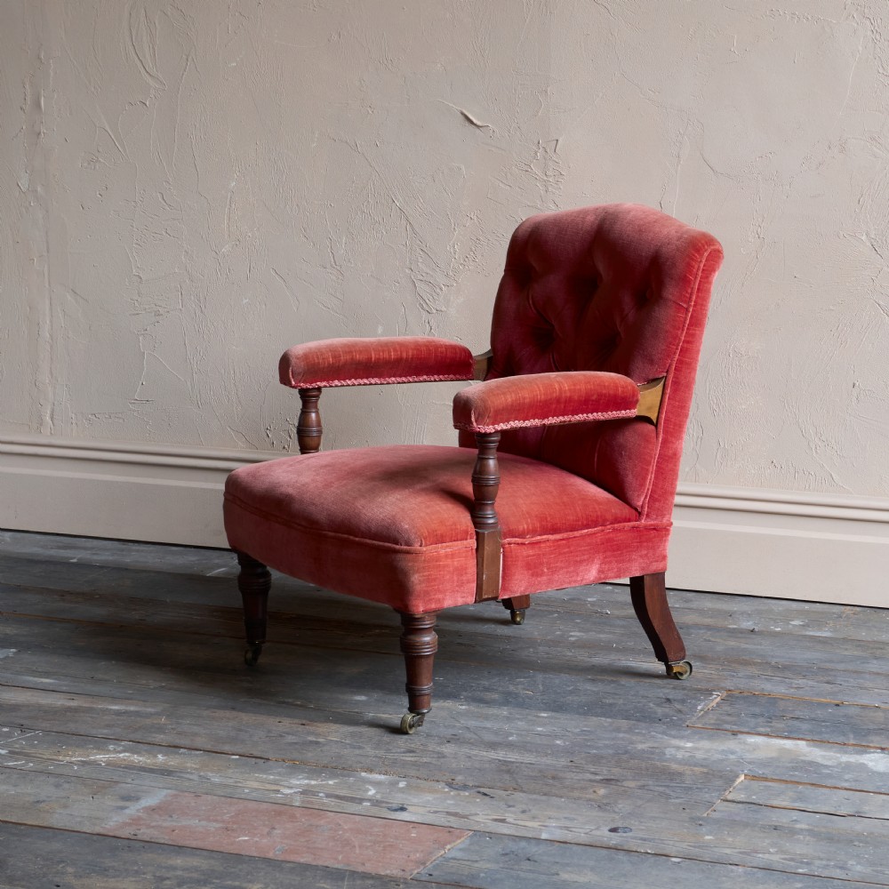 Victorian open armchair featuring deep buttoned rose pink velvet upholstery, turned wooden front legs, and brass castors. View VI