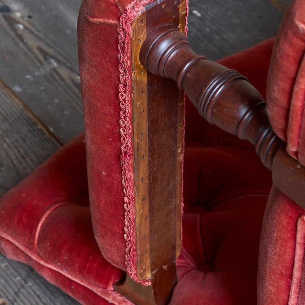 Victorian open armchair featuring deep buttoned rose pink velvet upholstery, turned wooden front legs, and brass castors. View X