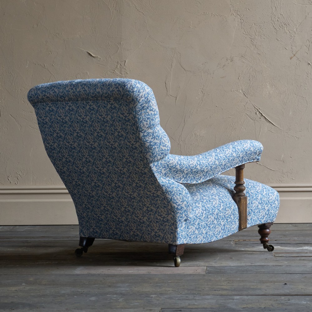 A low Victorian open armchair upholstered in a blue and white scroll pattern, featuring deep buttoning on the backrest, padded arms on turned wooden supports, and turned legs on castors. View VII