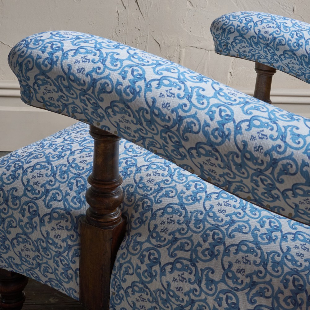 A low Victorian open armchair upholstered in a blue and white scroll pattern, featuring deep buttoning on the backrest, padded arms on turned wooden supports, and turned legs on castors. View II