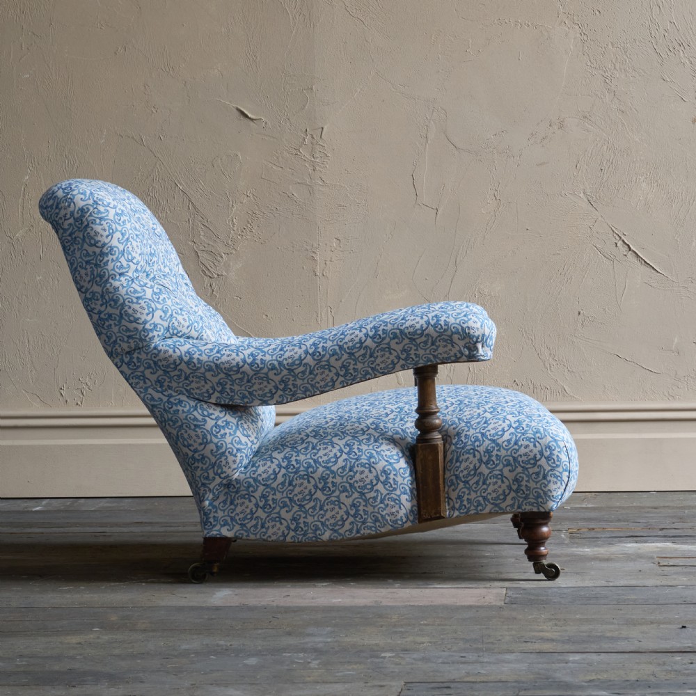 A low Victorian open armchair upholstered in a blue and white scroll pattern, featuring deep buttoning on the backrest, padded arms on turned wooden supports, and turned legs on castors. View III