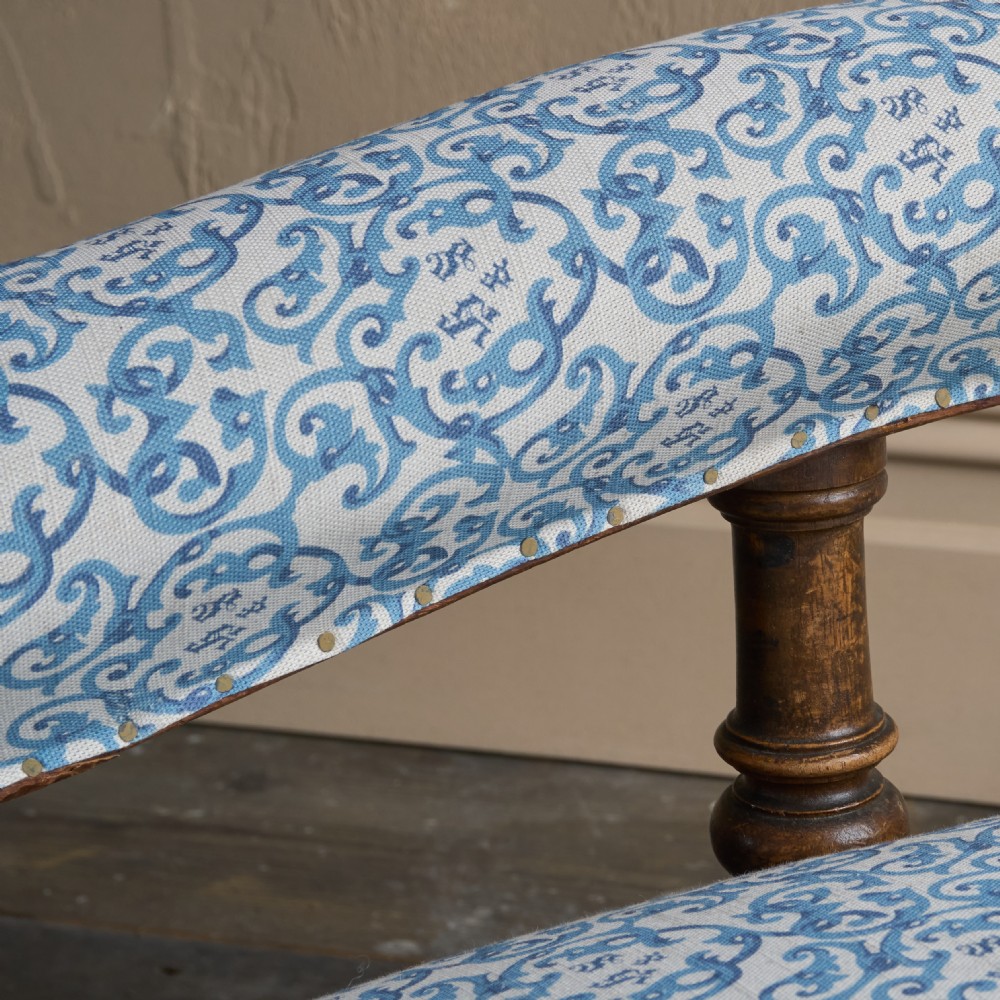A low Victorian open armchair upholstered in a blue and white scroll pattern, featuring deep buttoning on the backrest, padded arms on turned wooden supports, and turned legs on castors. View V