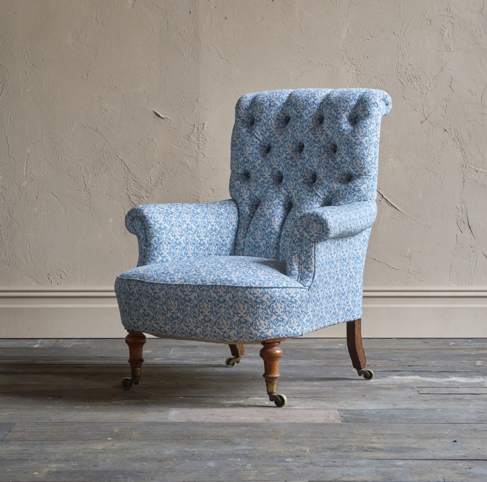 A Victorian button-back armchair upholstered in blue and white pattern printed ticking fabric with turned timber front legs on brass castors.