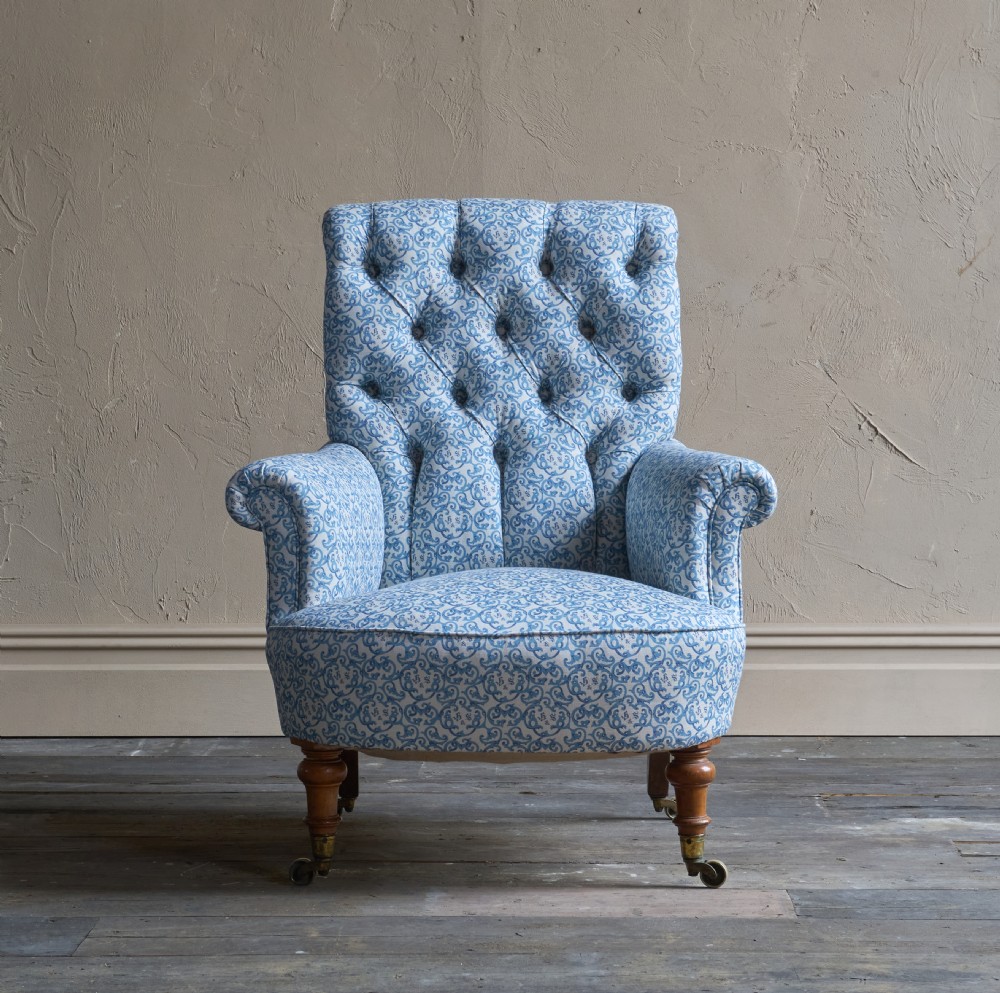 A Victorian button-back armchair upholstered in blue and white pattern printed ticking fabric with turned timber front legs on brass castors. View II