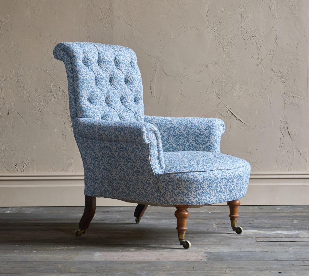 A Victorian button-back armchair upholstered in blue and white pattern printed ticking fabric with turned timber front legs on brass castors. View III