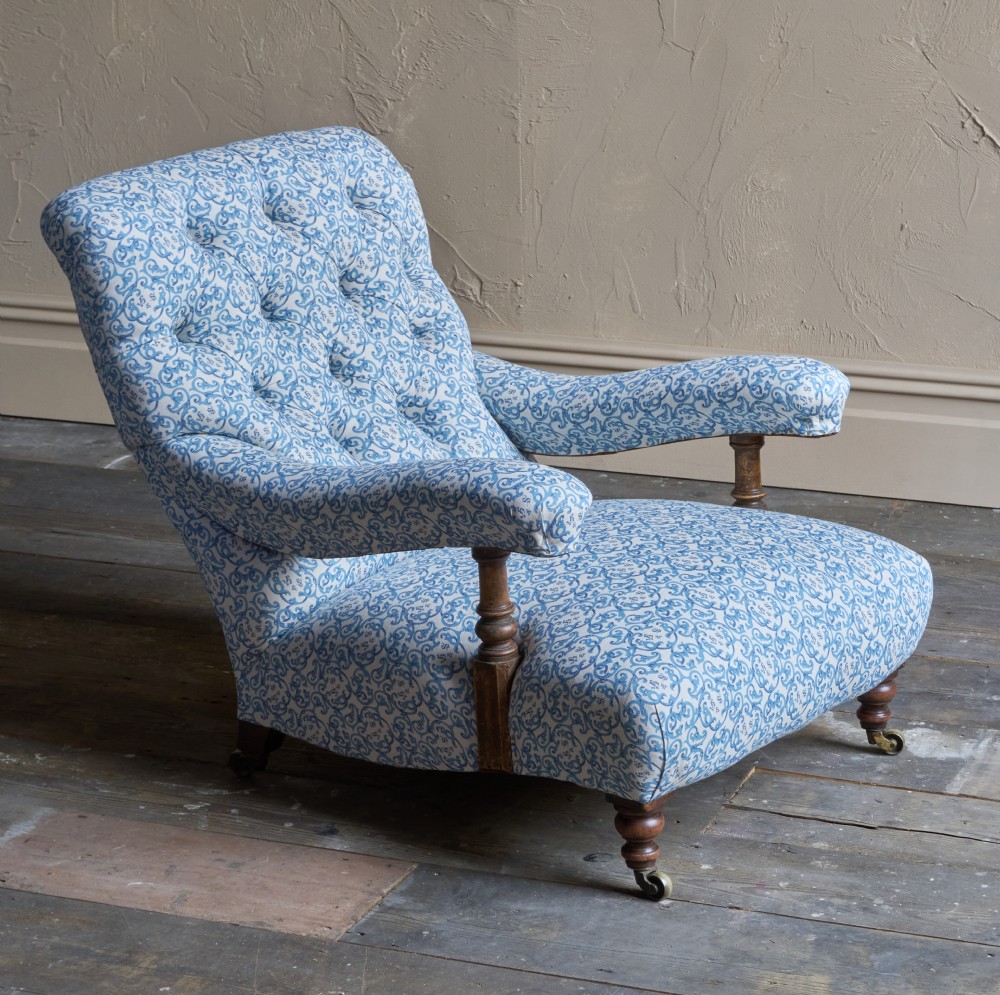 A low Victorian open armchair upholstered in a blue and white scroll pattern, featuring deep buttoning on the backrest, padded arms on turned wooden supports, and turned legs on castors. View VIII