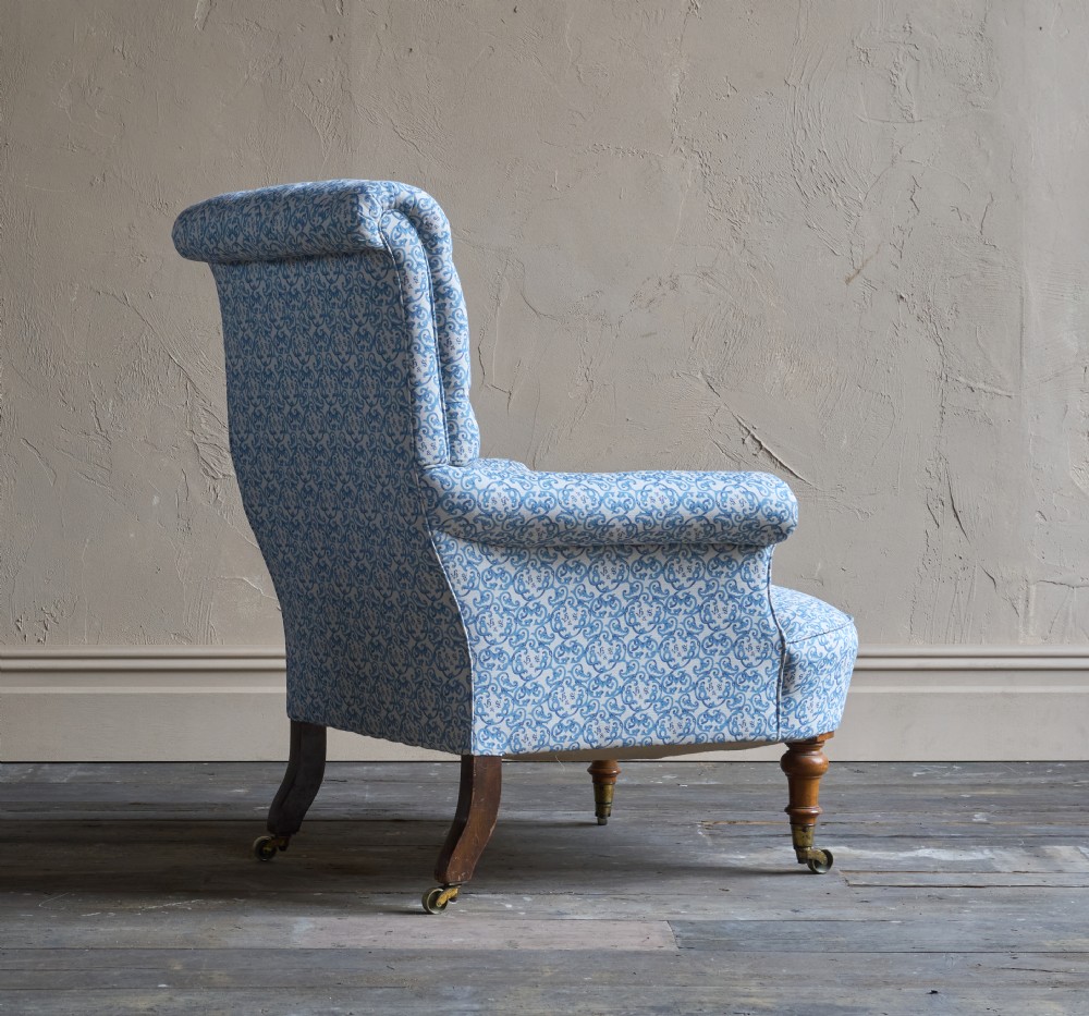 A Victorian button-back armchair upholstered in blue and white pattern printed ticking fabric with turned timber front legs on brass castors. View V