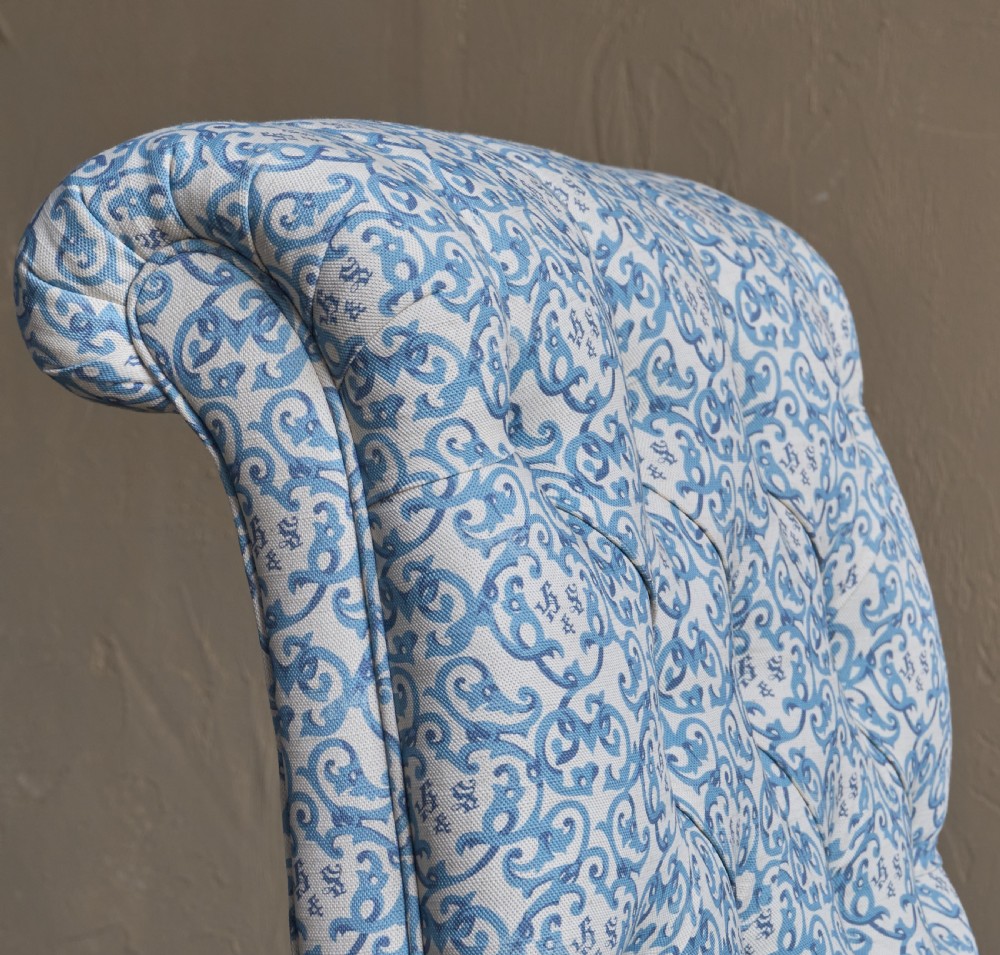 A Victorian button-back armchair upholstered in blue and white pattern printed ticking fabric with turned timber front legs on brass castors. View VI