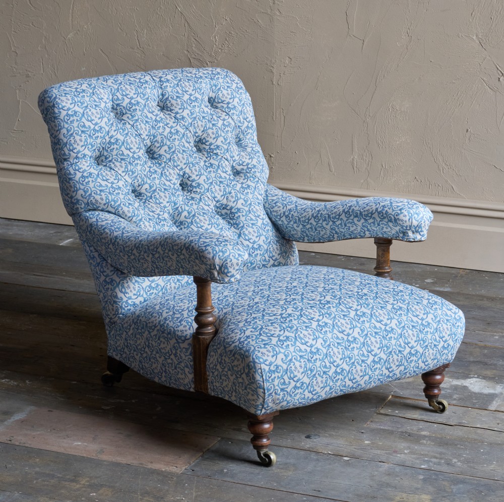 A low Victorian open armchair upholstered in a blue and white scroll pattern, featuring deep buttoning on the backrest, padded arms on turned wooden supports, and turned legs on castors. View IX