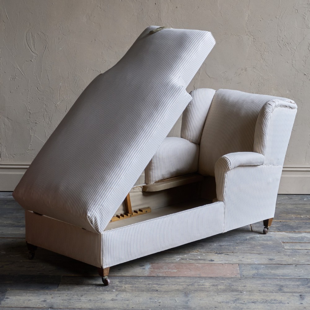 An upholstered antique chaise longue covered in off-white fabric with fine vertical stripes, featuring castors and a single high armrest. View III