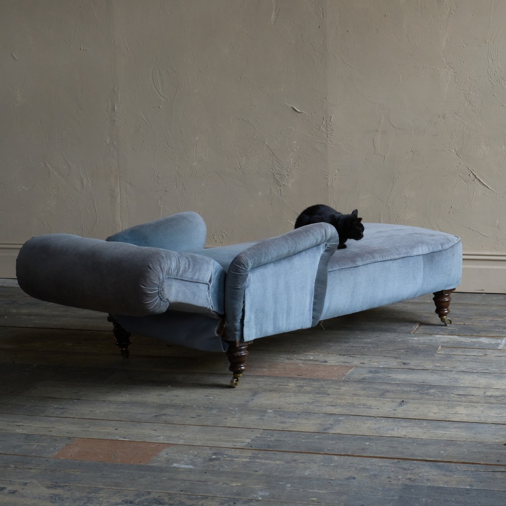 A Victorian slate blue velvet upholstered reclining day bed with a tufted backrest, turned wood legs, and brass castors. View V