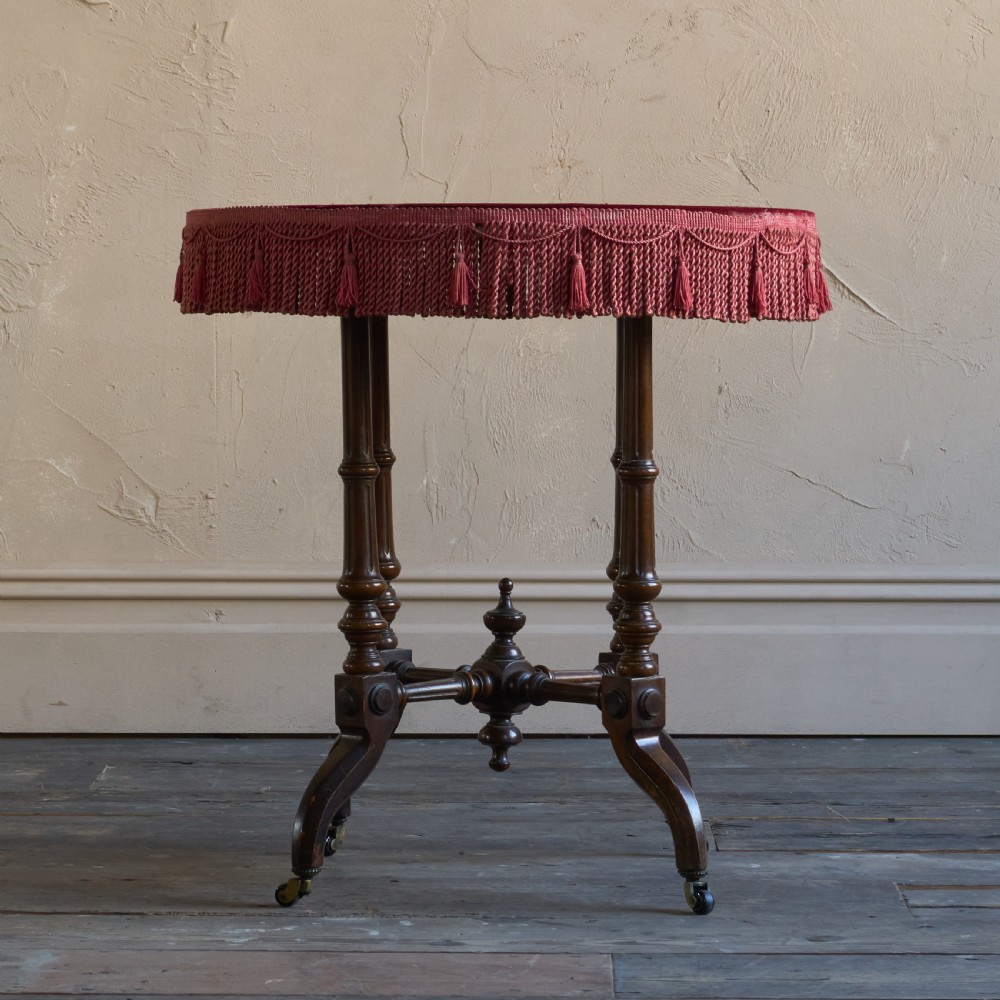 A round wooden side table with a deep red velvet top and fringed edge, supported by turned legs and castors. View II