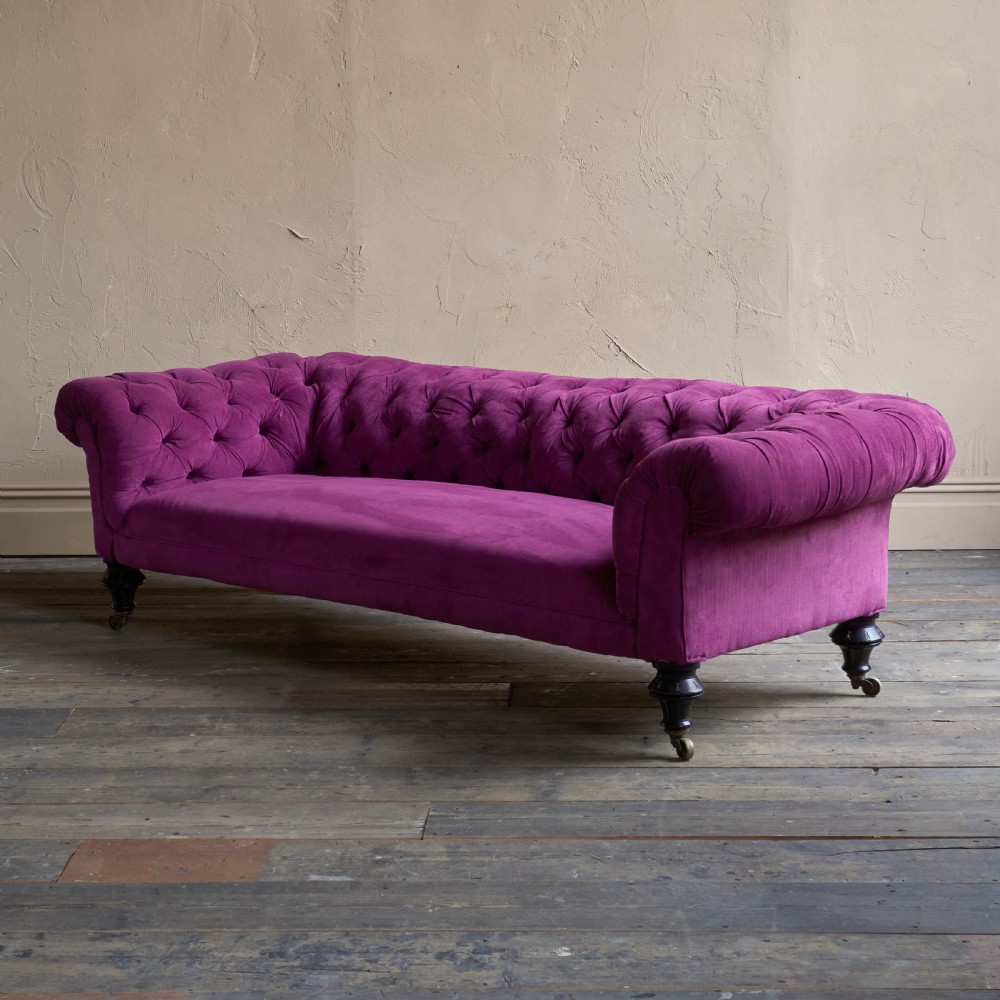 An antique velvet Chesterfield sofa featuring deep button tufting, rolled arms, and dark turned wooden legs with brass castors. View III