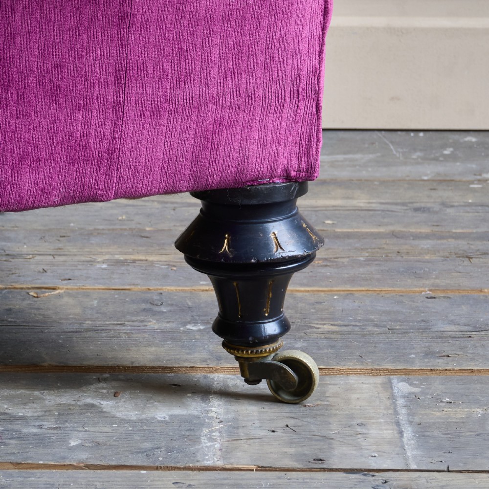 An antique velvet Chesterfield sofa featuring deep button tufting, rolled arms, and dark turned wooden legs with brass castors. View VI
