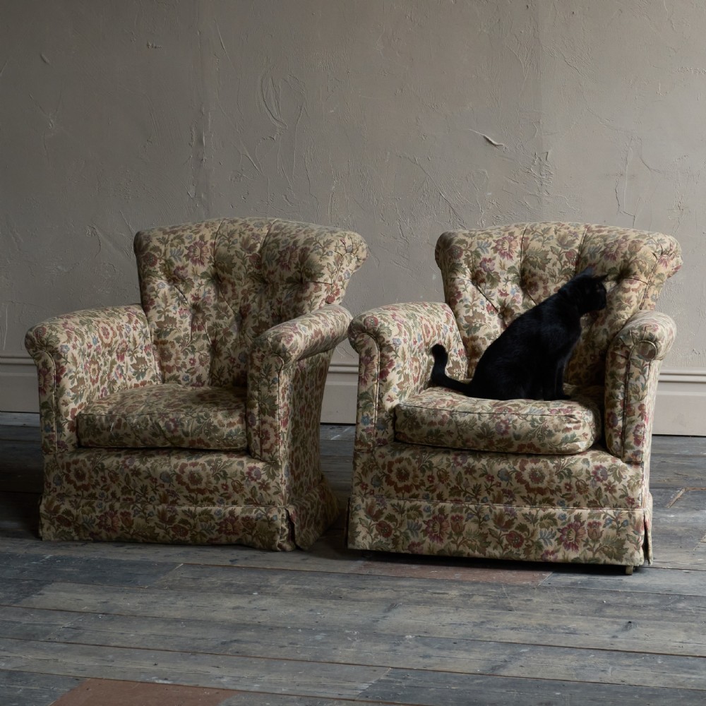 A pair of low-slung armchairs with deep-buttoned backrests, upholstered in a floral patterned fabric with rolled arms and skirted bases. View III