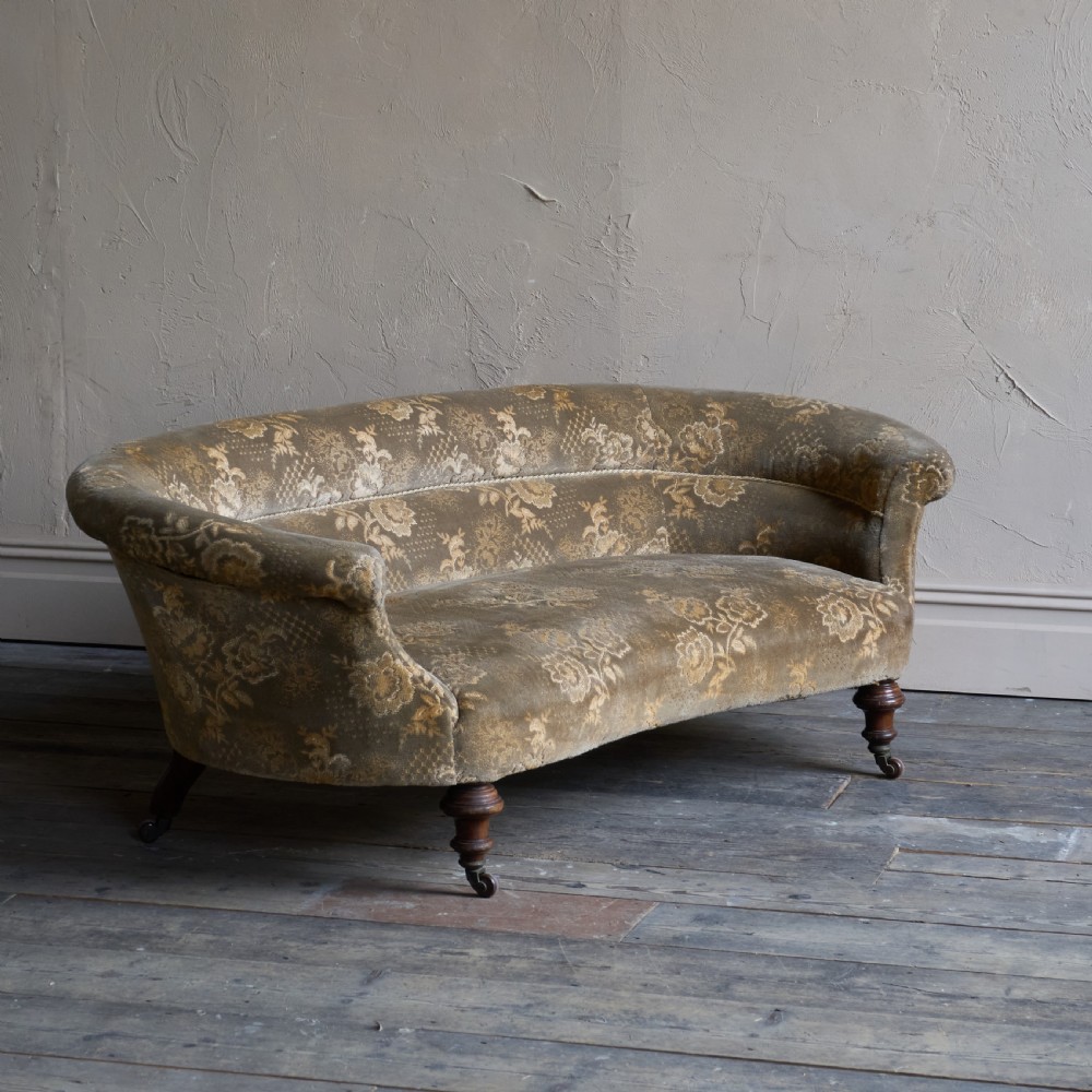 An antique kidney-shaped sofa upholstered in patterned brown fabric with turned wooden legs and castors.