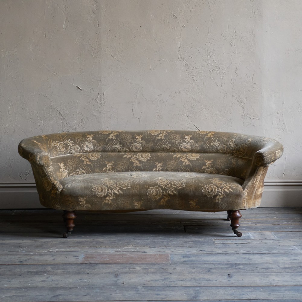 An antique kidney-shaped sofa upholstered in patterned brown fabric with turned wooden legs and castors. View II