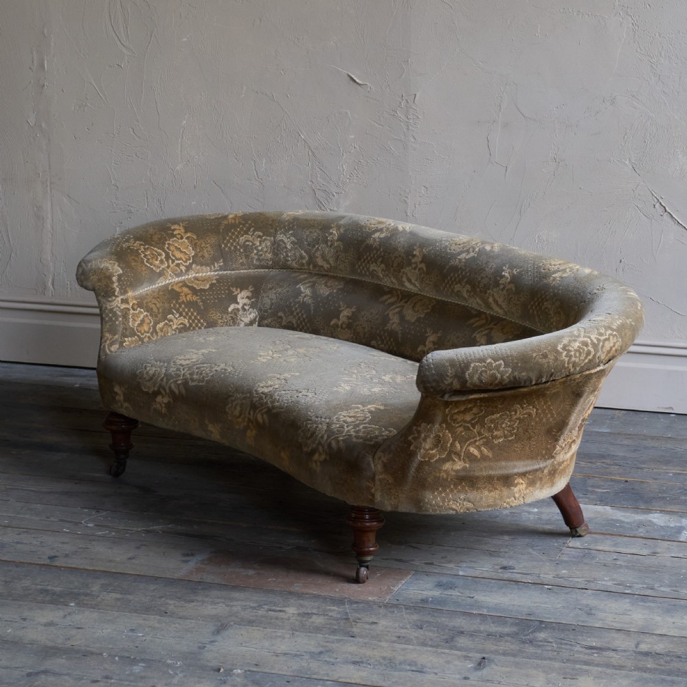 An antique kidney-shaped sofa upholstered in patterned brown fabric with turned wooden legs and castors. View III