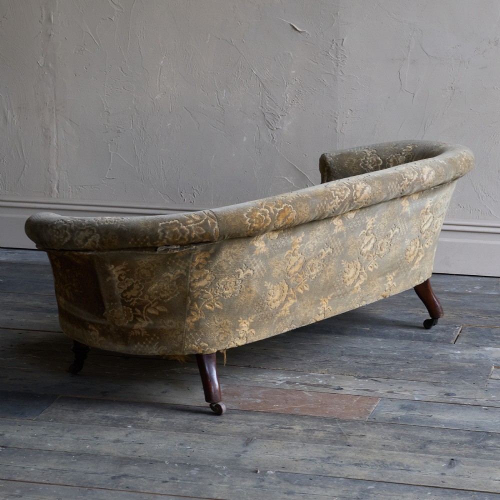 An antique kidney-shaped sofa upholstered in patterned brown fabric with turned wooden legs and castors. View IV