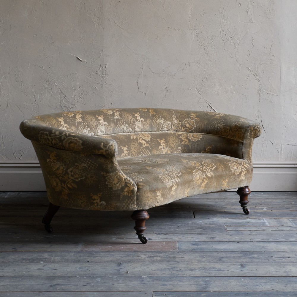 An antique kidney-shaped sofa upholstered in patterned brown fabric with turned wooden legs and castors. View V