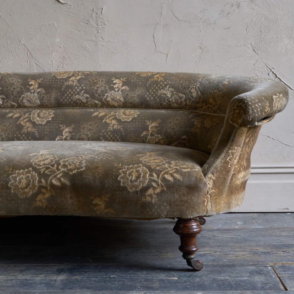 An antique kidney-shaped sofa upholstered in patterned brown fabric with turned wooden legs and castors. View VI