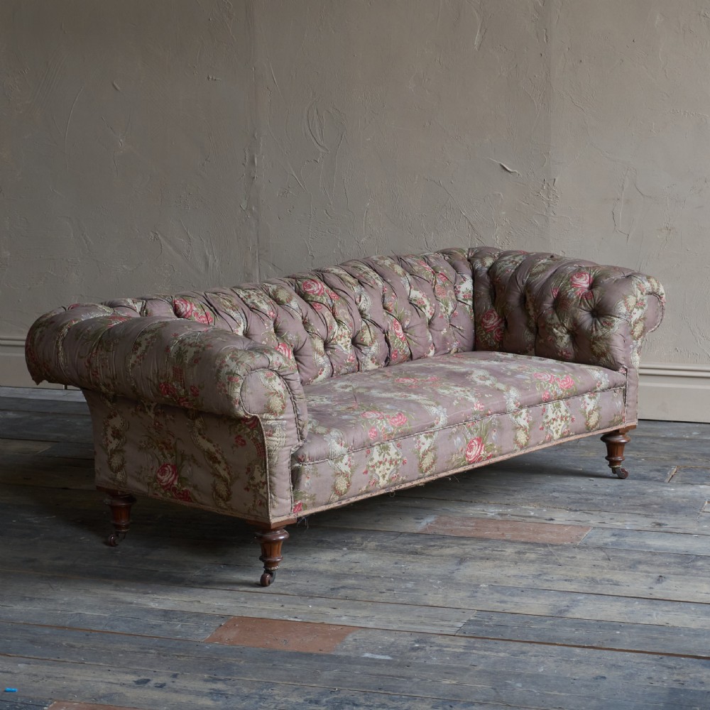 A Victorian deep-buttoned Chesterfield sofa upholstered in a floral fabric with rolled arms and turned mahogany legs on brass castors.
