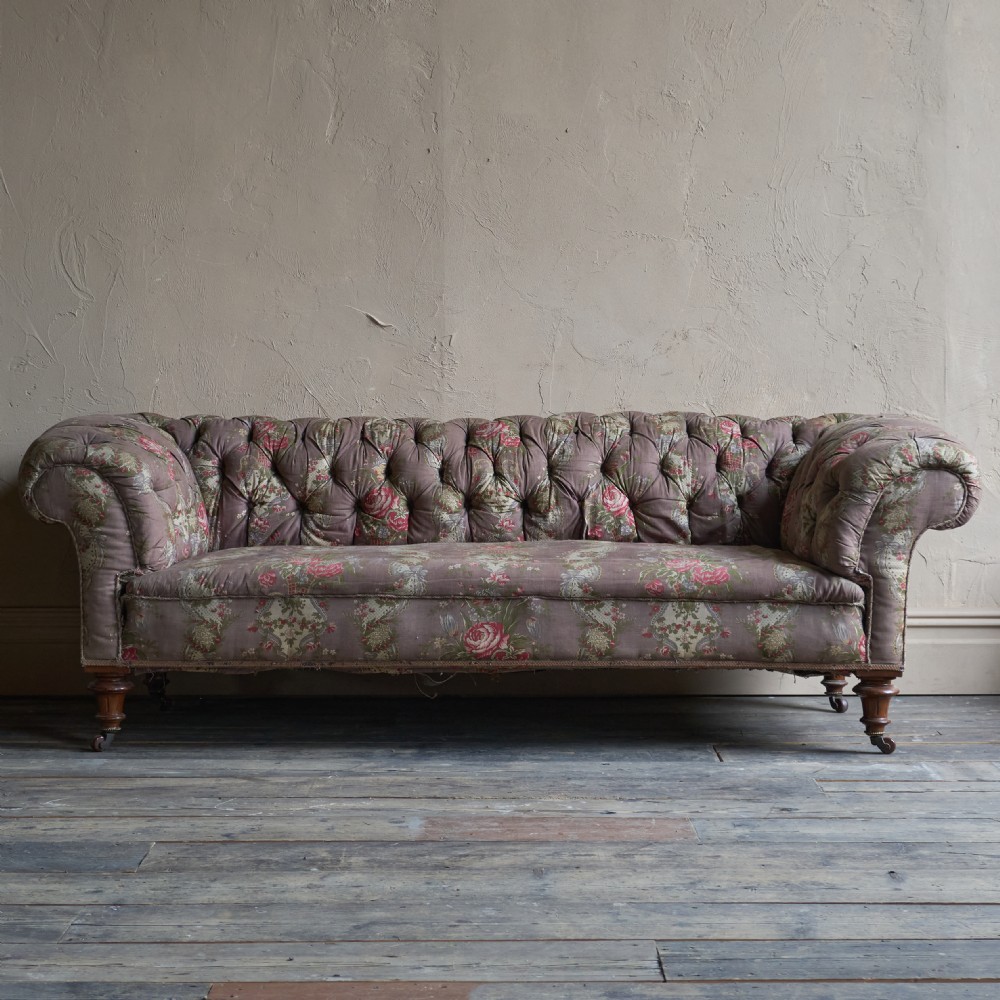 A Victorian deep-buttoned Chesterfield sofa upholstered in a floral fabric with rolled arms and turned mahogany legs on brass castors. View II