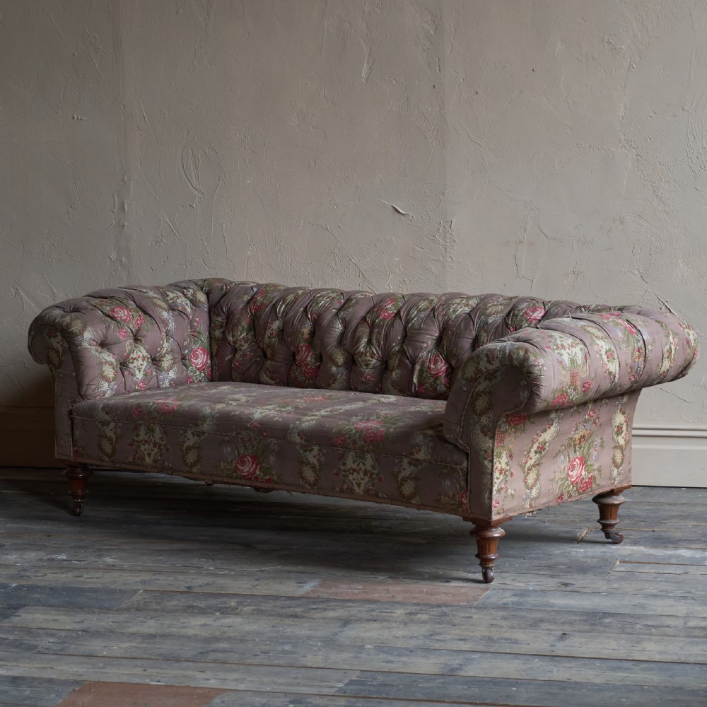 A Victorian deep-buttoned Chesterfield sofa upholstered in a floral fabric with rolled arms and turned mahogany legs on brass castors. View III