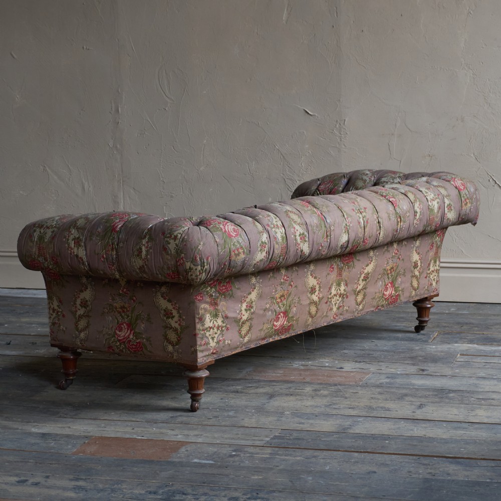 A Victorian deep-buttoned Chesterfield sofa upholstered in a floral fabric with rolled arms and turned mahogany legs on brass castors. View V
