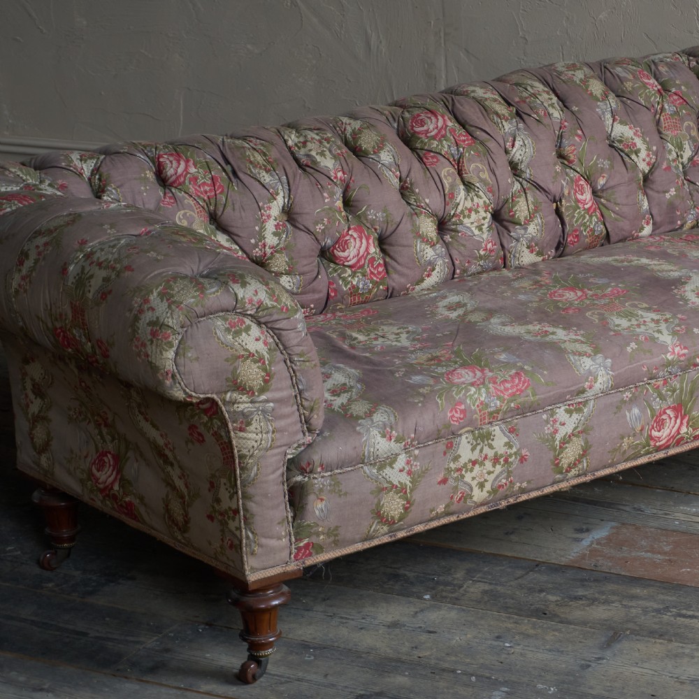 A Victorian deep-buttoned Chesterfield sofa upholstered in a floral fabric with rolled arms and turned mahogany legs on brass castors. View VI