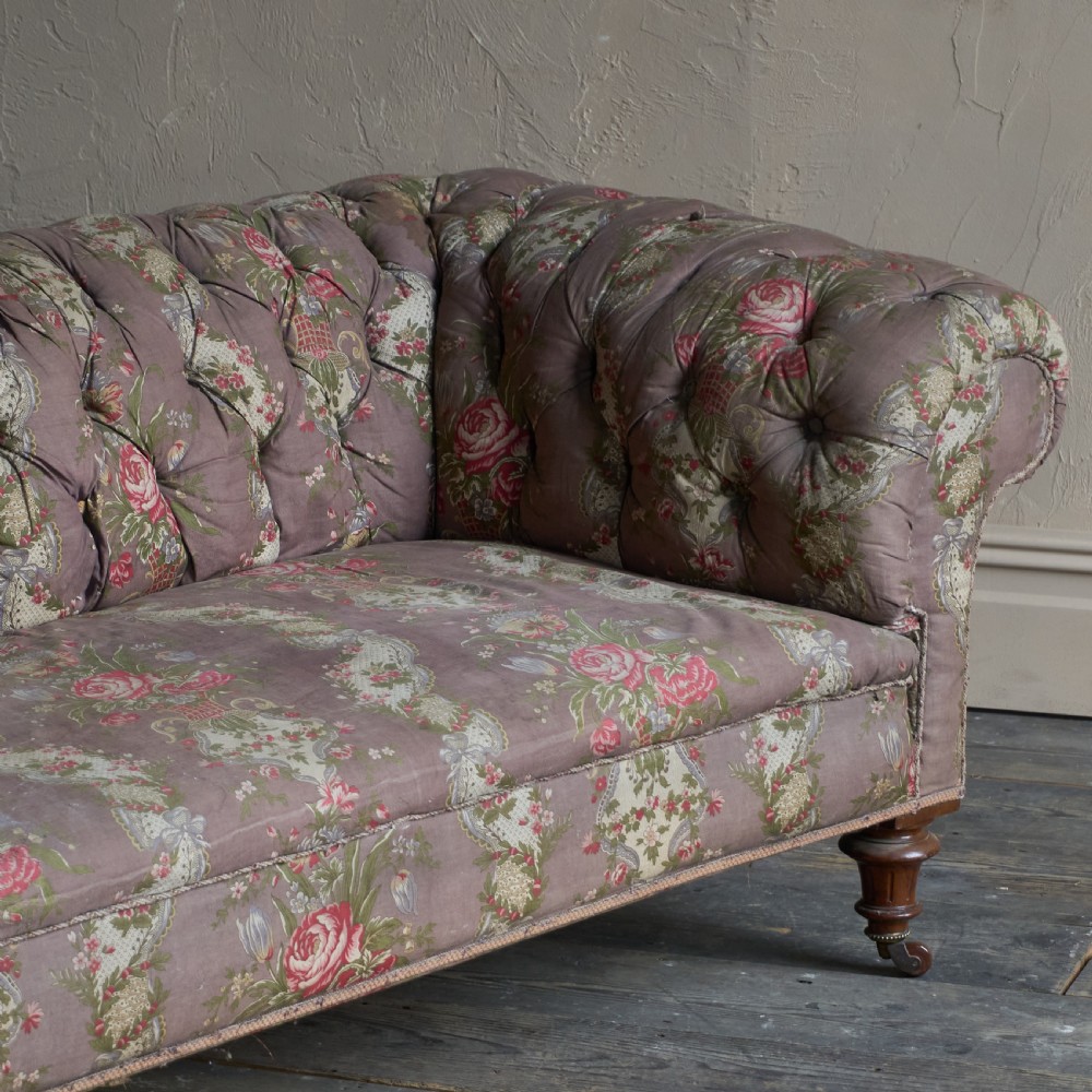 A Victorian deep-buttoned Chesterfield sofa upholstered in a floral fabric with rolled arms and turned mahogany legs on brass castors. View VII