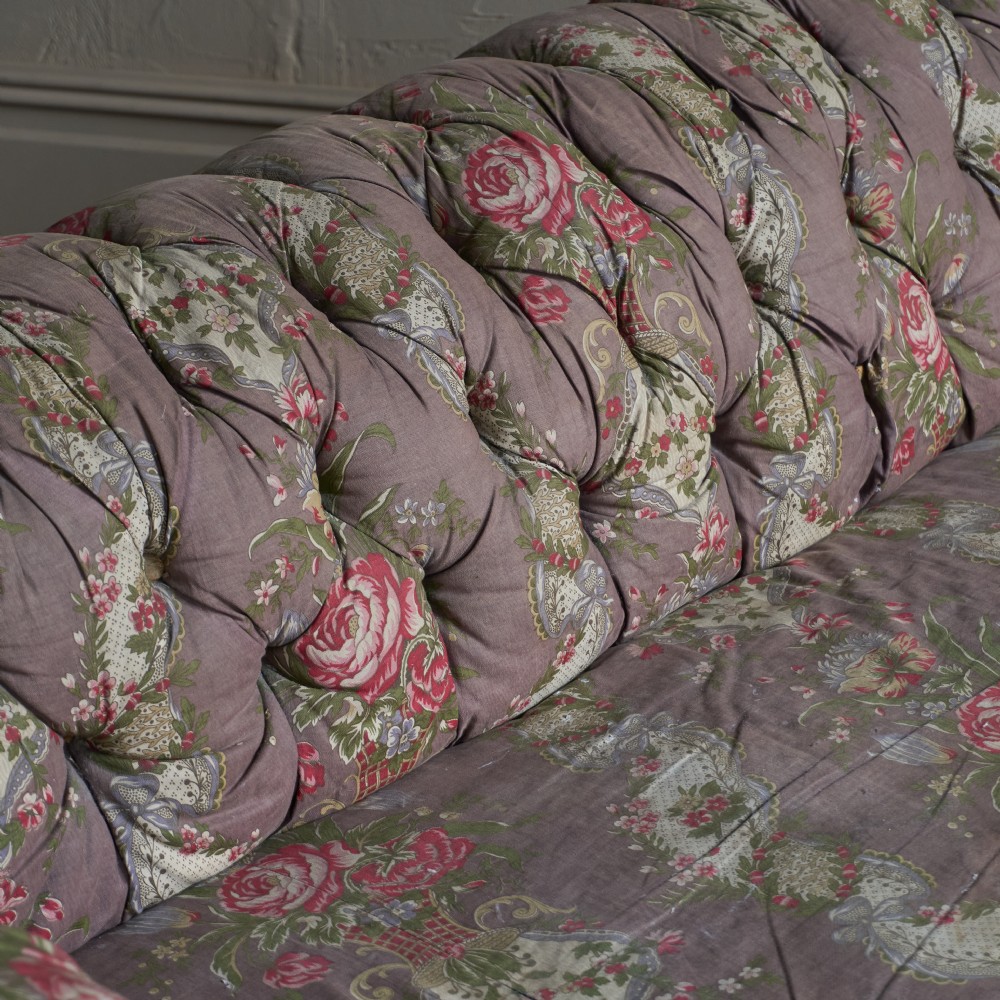 A Victorian deep-buttoned Chesterfield sofa upholstered in a floral fabric with rolled arms and turned mahogany legs on brass castors. View VIII