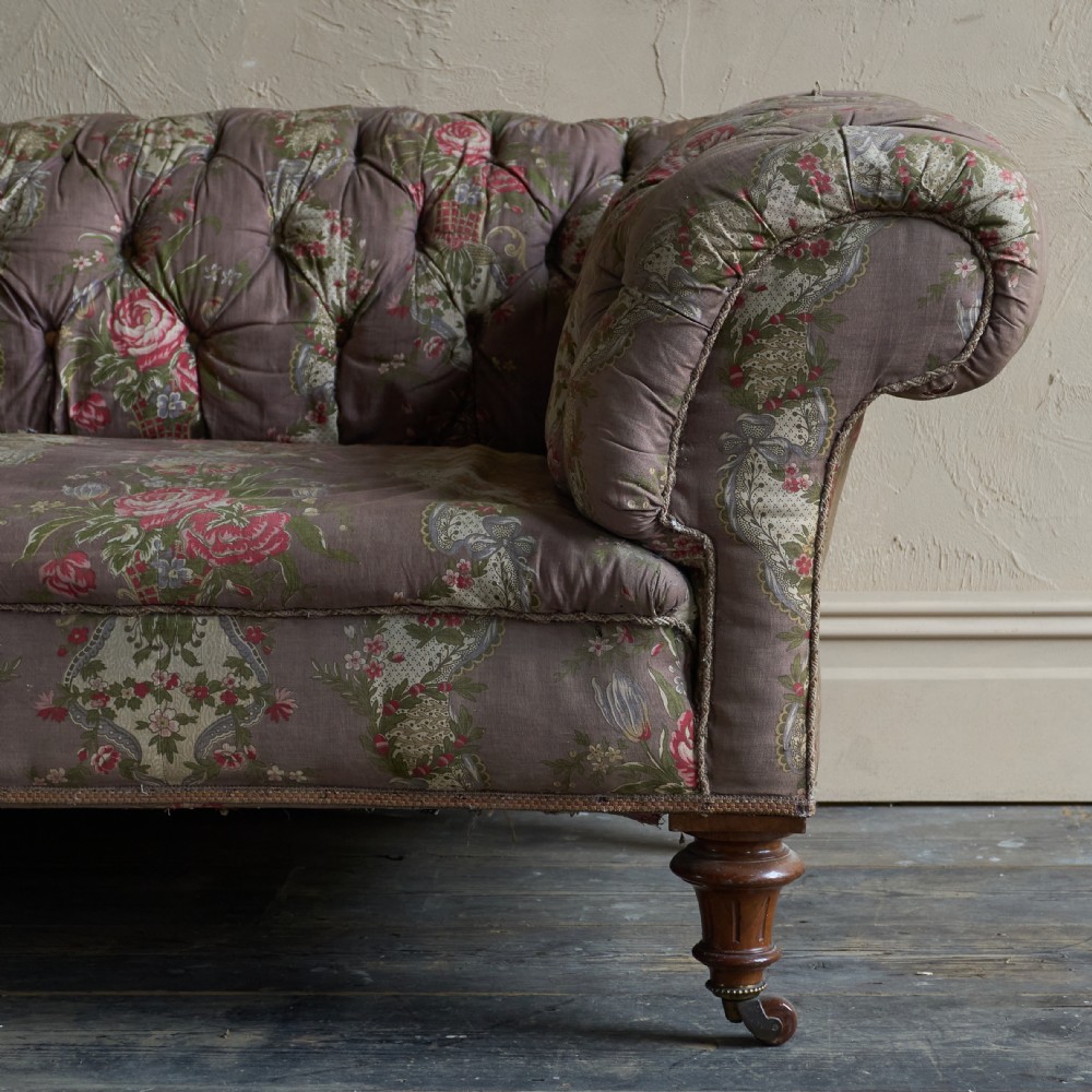 A Victorian deep-buttoned Chesterfield sofa upholstered in a floral fabric with rolled arms and turned mahogany legs on brass castors. View XI
