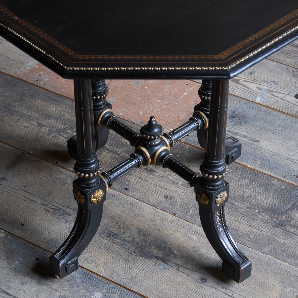 An octagonal ebonised side table featuring turned legs with gilt accents, central stretchers with carved rosettes, and brass castors. View II