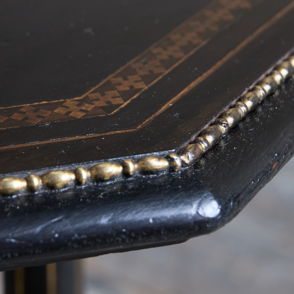 An octagonal ebonised side table featuring turned legs with gilt accents, central stretchers with carved rosettes, and brass castors. View V