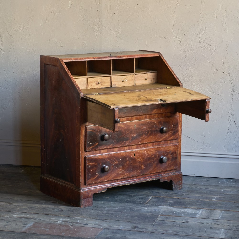 An antique wood bureau with a faux mahogany grain finish featuring a drop-down writing flap, internal pigeonholes, and three lower drawers with round turned handles.