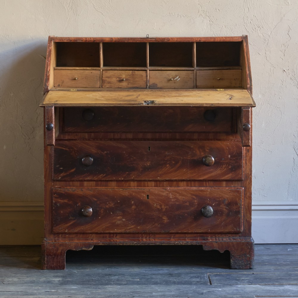 An antique wood bureau with a faux mahogany grain finish featuring a drop-down writing flap, internal pigeonholes, and three lower drawers with round turned handles. View III