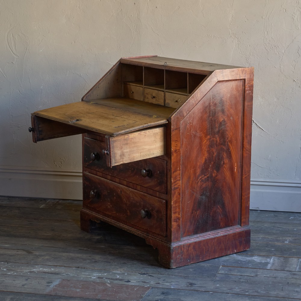An antique wood bureau with a faux mahogany grain finish featuring a drop-down writing flap, internal pigeonholes, and three lower drawers with round turned handles. View V