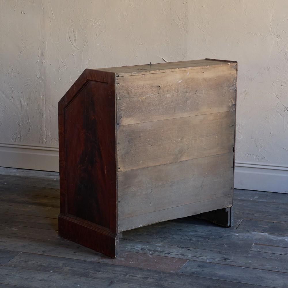 An antique wood bureau with a faux mahogany grain finish featuring a drop-down writing flap, internal pigeonholes, and three lower drawers with round turned handles. View VI