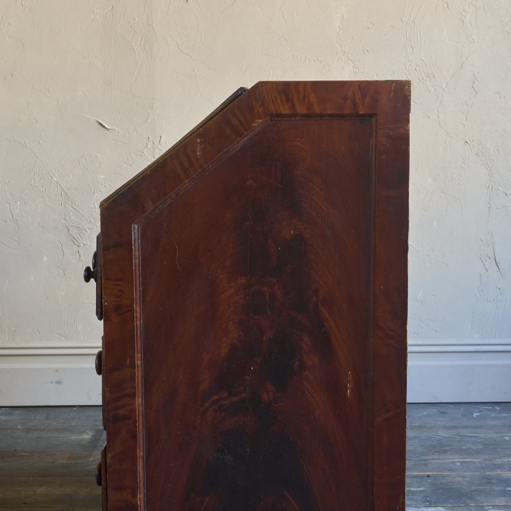An antique wood bureau with a faux mahogany grain finish featuring a drop-down writing flap, internal pigeonholes, and three lower drawers with round turned handles. View VII