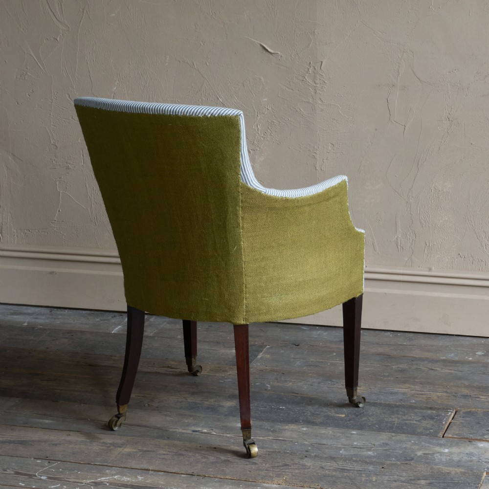 An antique George III library armchair upholstered in blue-striped fabric with contrasting yellow side panels and dark reeded wooden legs with brass castors. View II