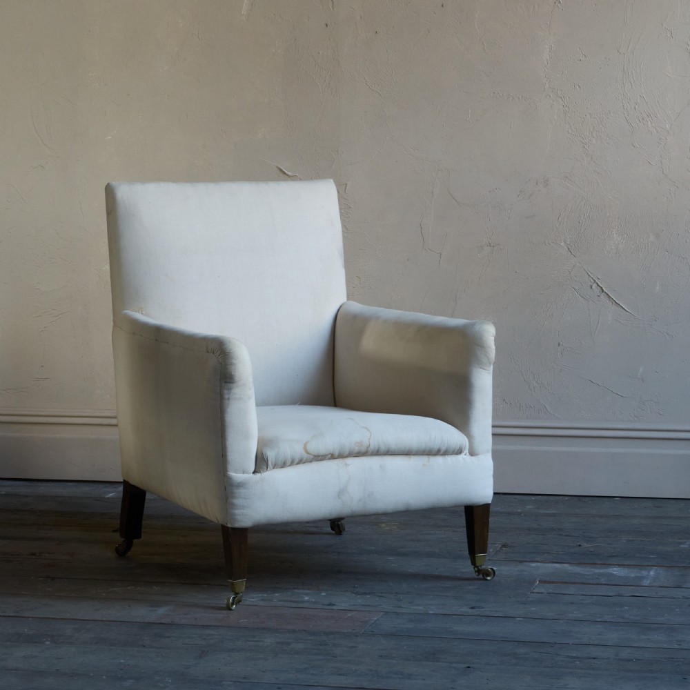An Edwardian calico-covered library armchair with low wooden legs and brass castors, shown against a plain wall. View VI