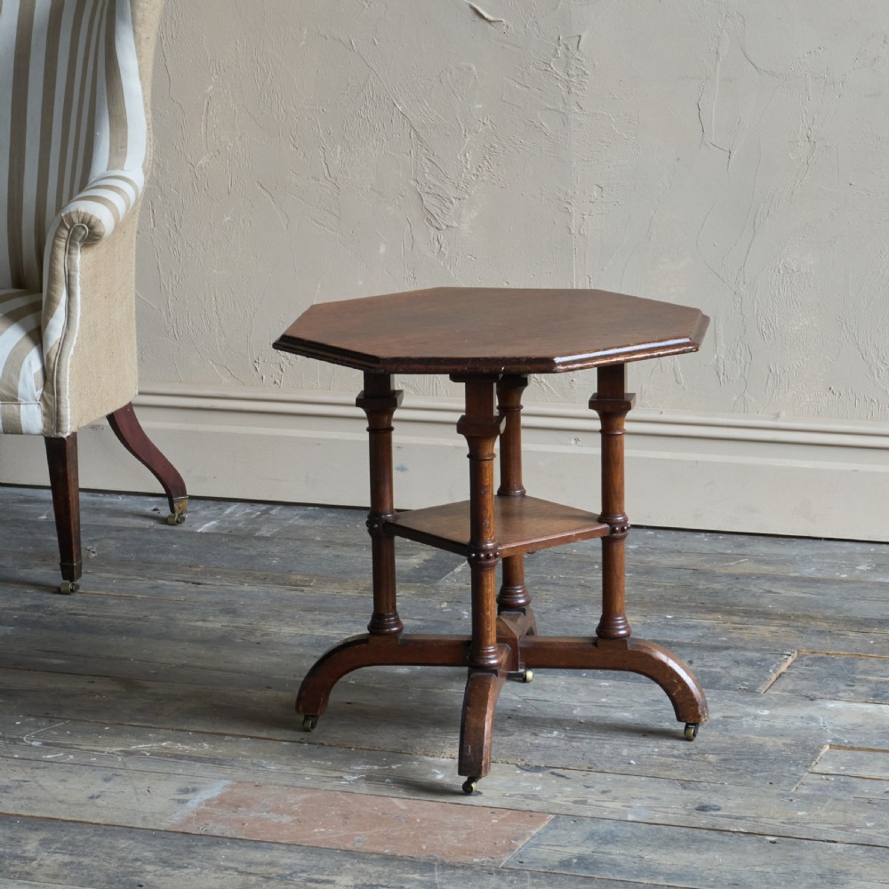 An octagonal Victorian walnut side table featuring turned legs, a lower tier shelf, and brass castors on curved feet. View III