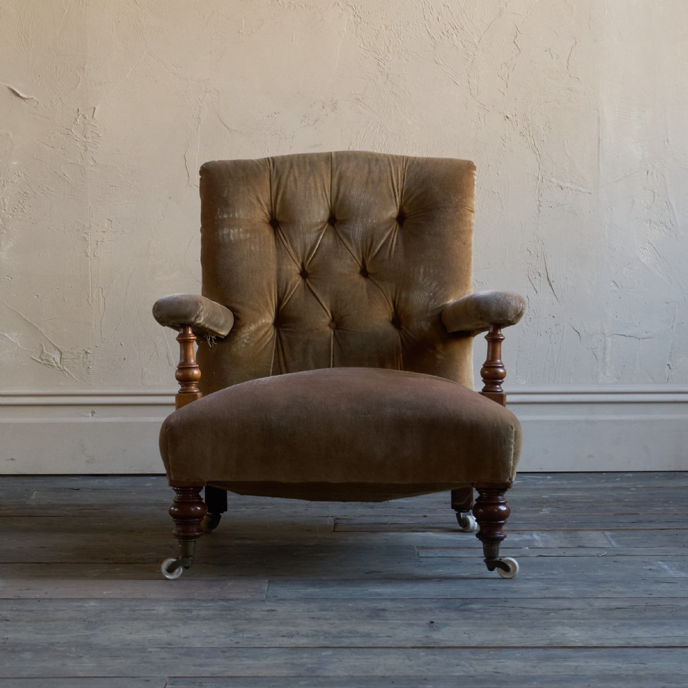 An antique open armchair upholstered in golden brown velvet featuring button-tufting, turned wooden front legs, and castors. View II