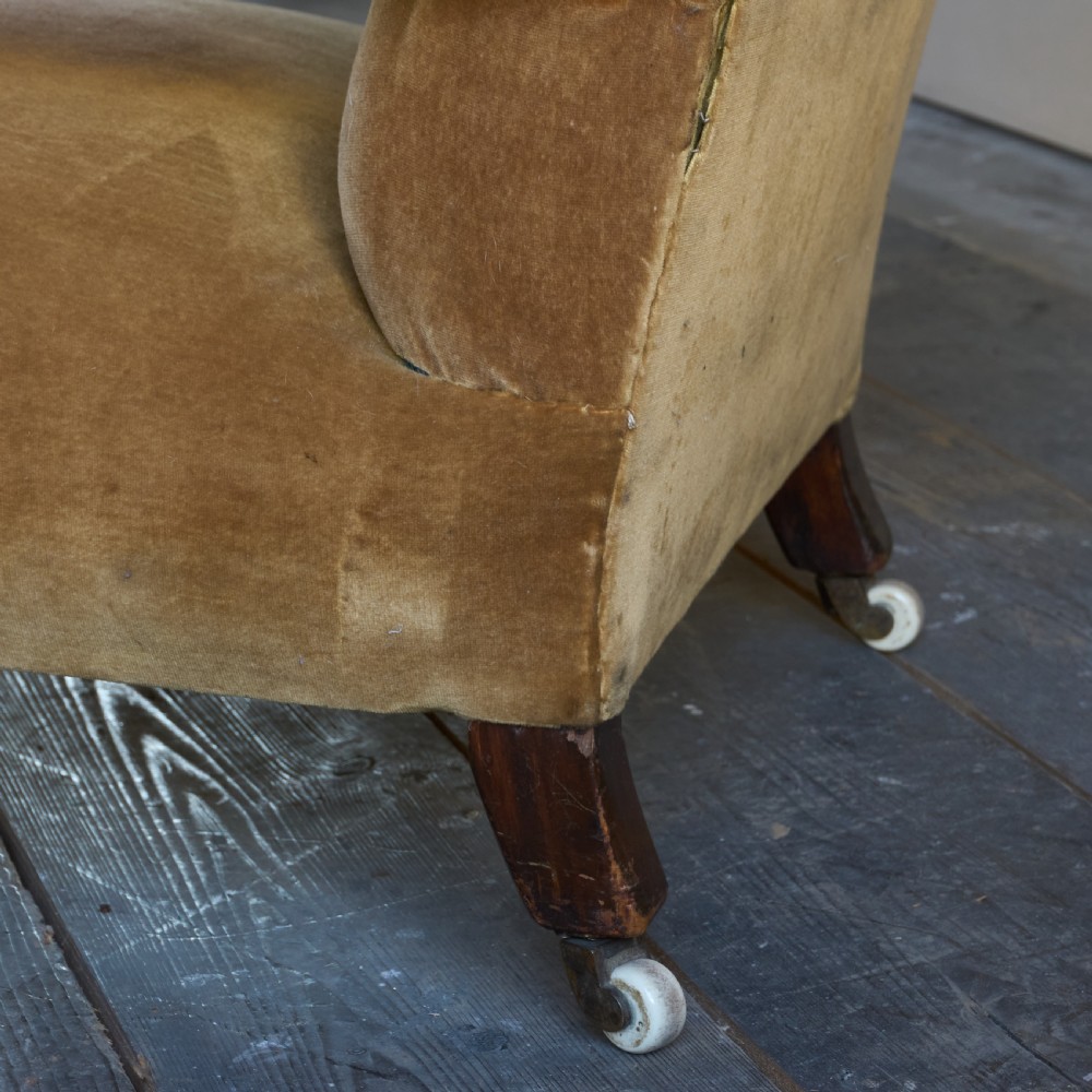 An antique open armchair upholstered in golden brown velvet featuring button-tufting, turned wooden front legs, and castors. View V